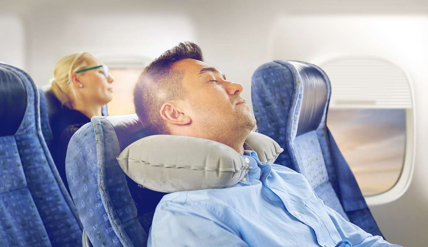 Passenger sleeping on a long-haul flight using a travel neck pillow and eye mask to improve sleep quality in economy class.