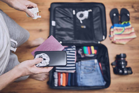 Collection of innovative travel gadgets laid out including a portable charger, packing cube, travel adapter and noise-cancelling earbuds.
