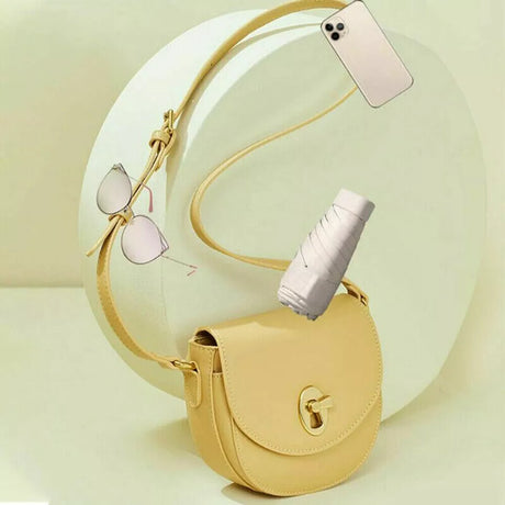 Folded travel umbrella beside a yellow handbag, sunglasses and phone